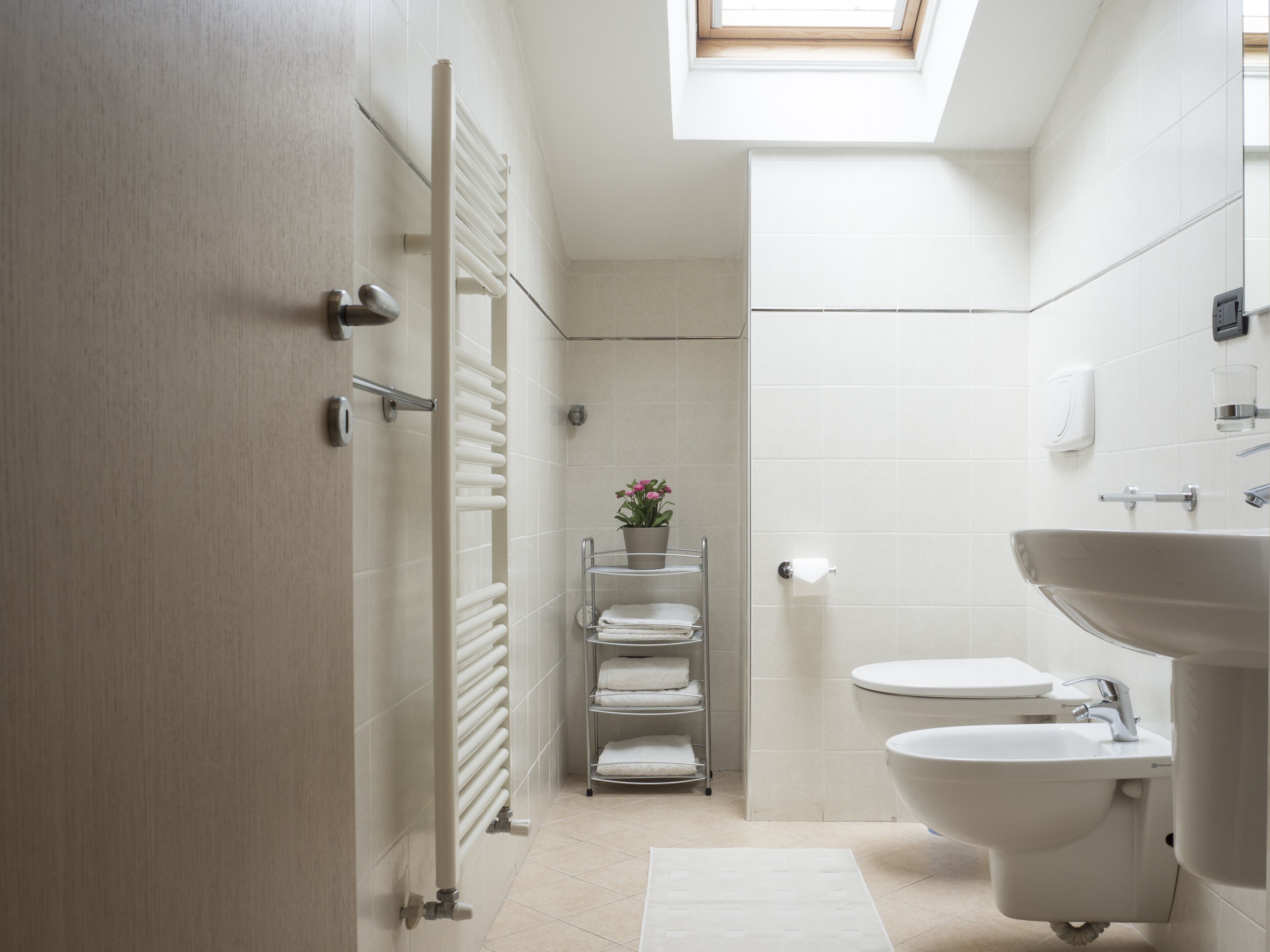 Un baño moderno con tragaluz, bañera, lavamanos y un toallero con varias toallas.