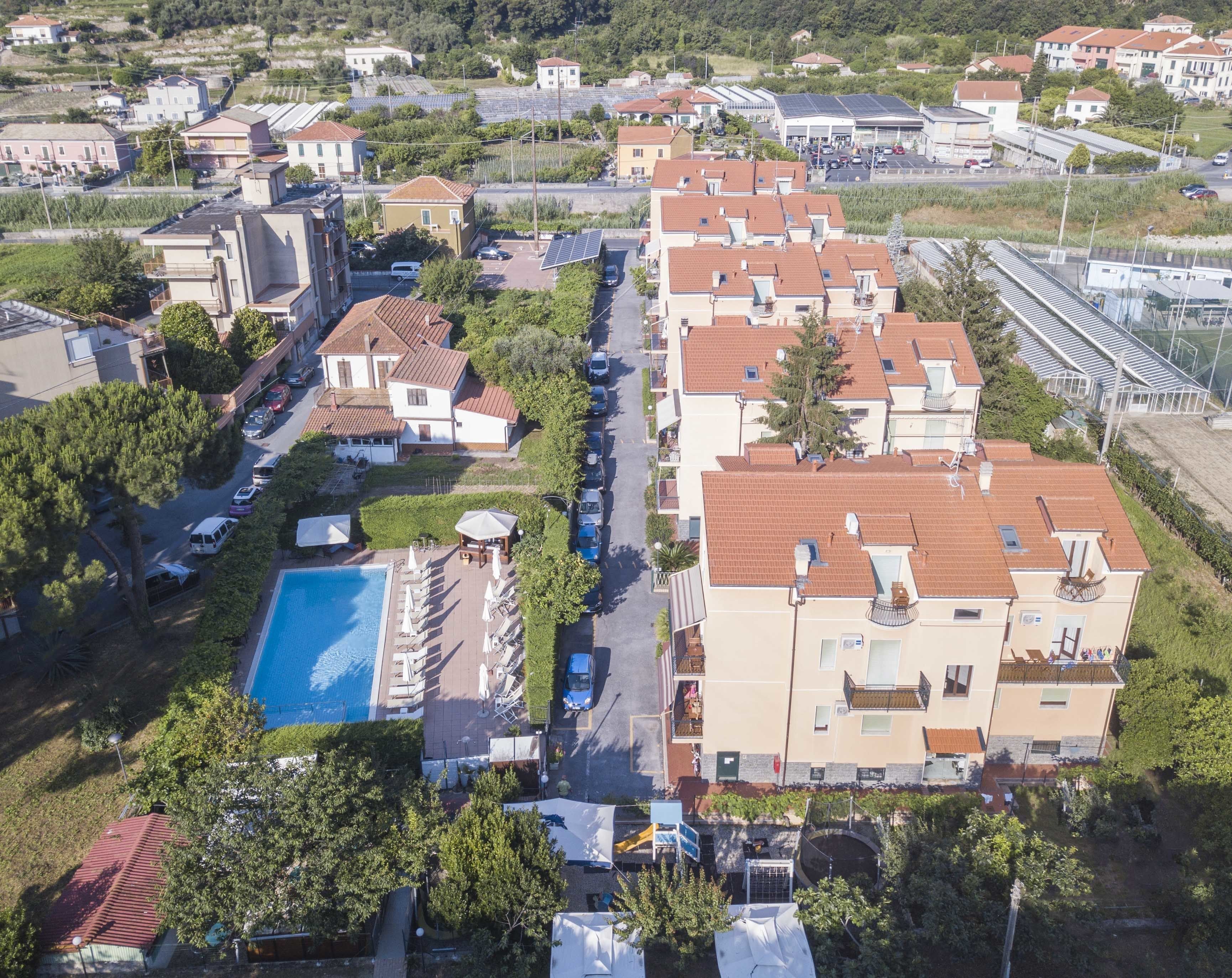 An aerial view of a residential area with multiple houses, a swimming pool, and solar panels.