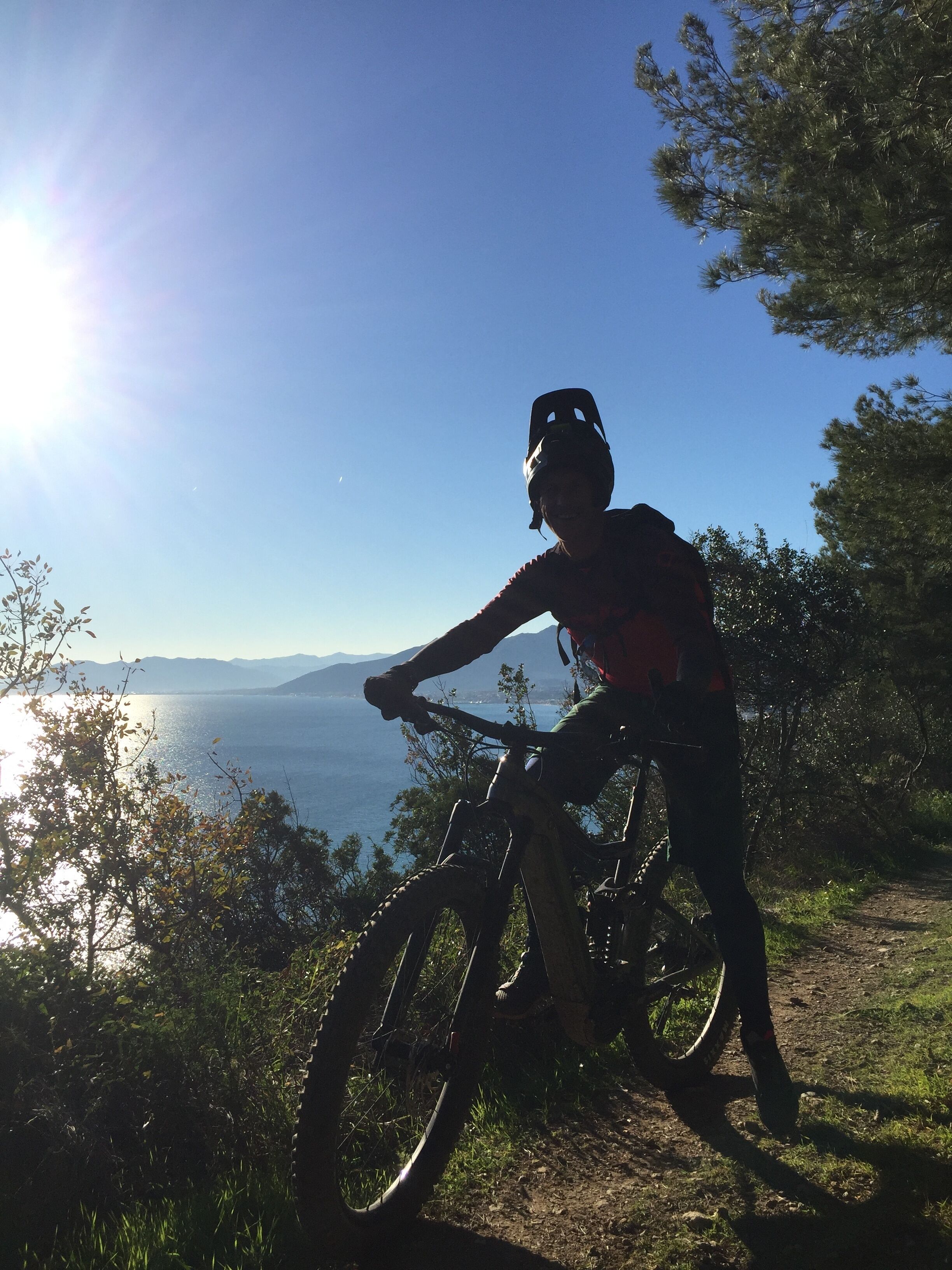A mountain biker on a trail with a scenic view of a lake and mountains in the background.