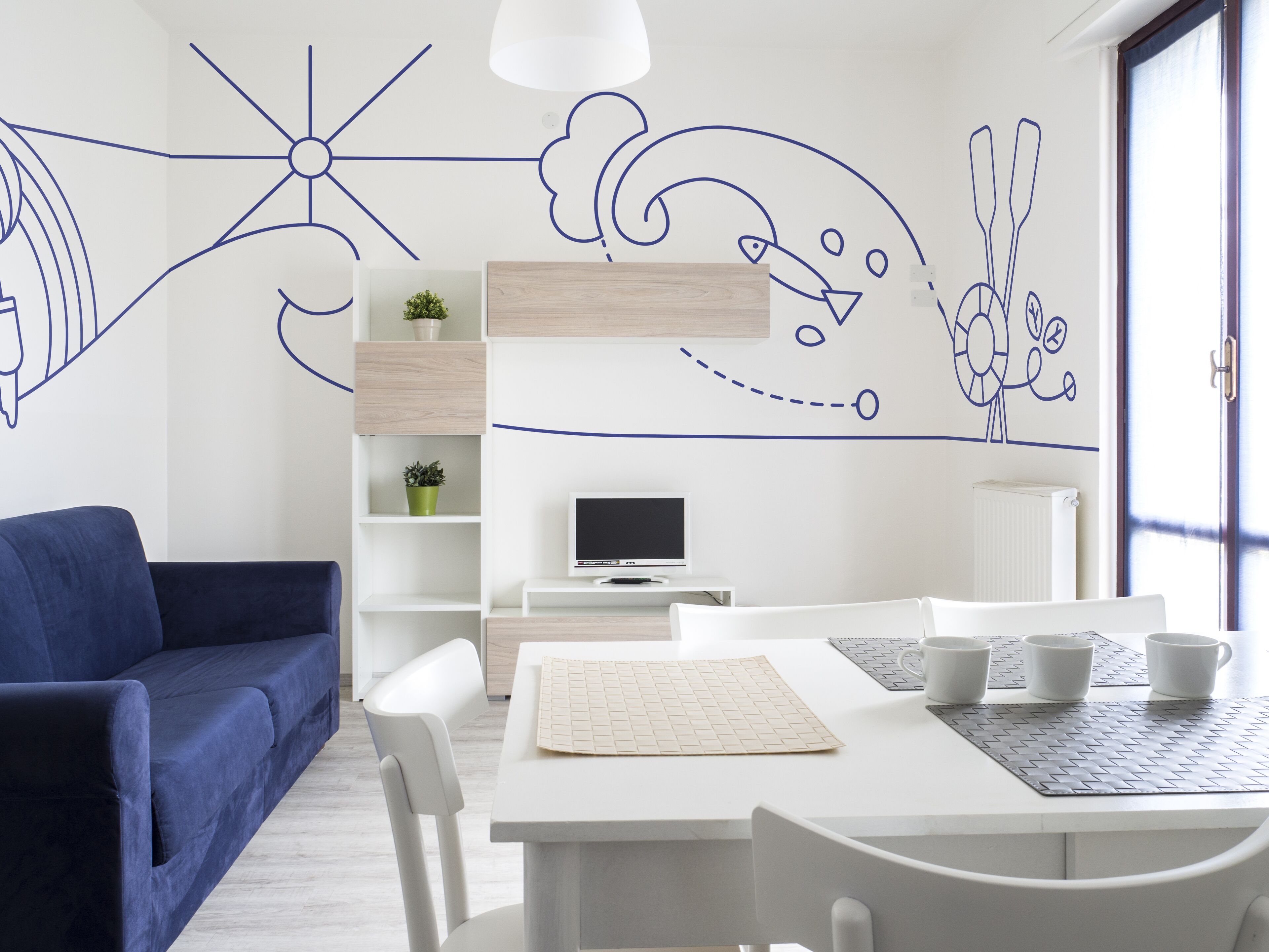 A modern living room with a blue sofa, white dining table, and a TV.