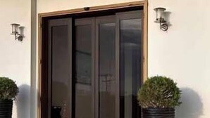 A hotel entrance with a glass door, metal railings, and two potted plants. - Byzantio Hotel (Pavlos Melas)
