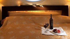 A bed with a floral bedspread, a bottle of wine, a glass of wine, and a plate of food on a tray. - Byzantio Hotel (Pavlos Melas)