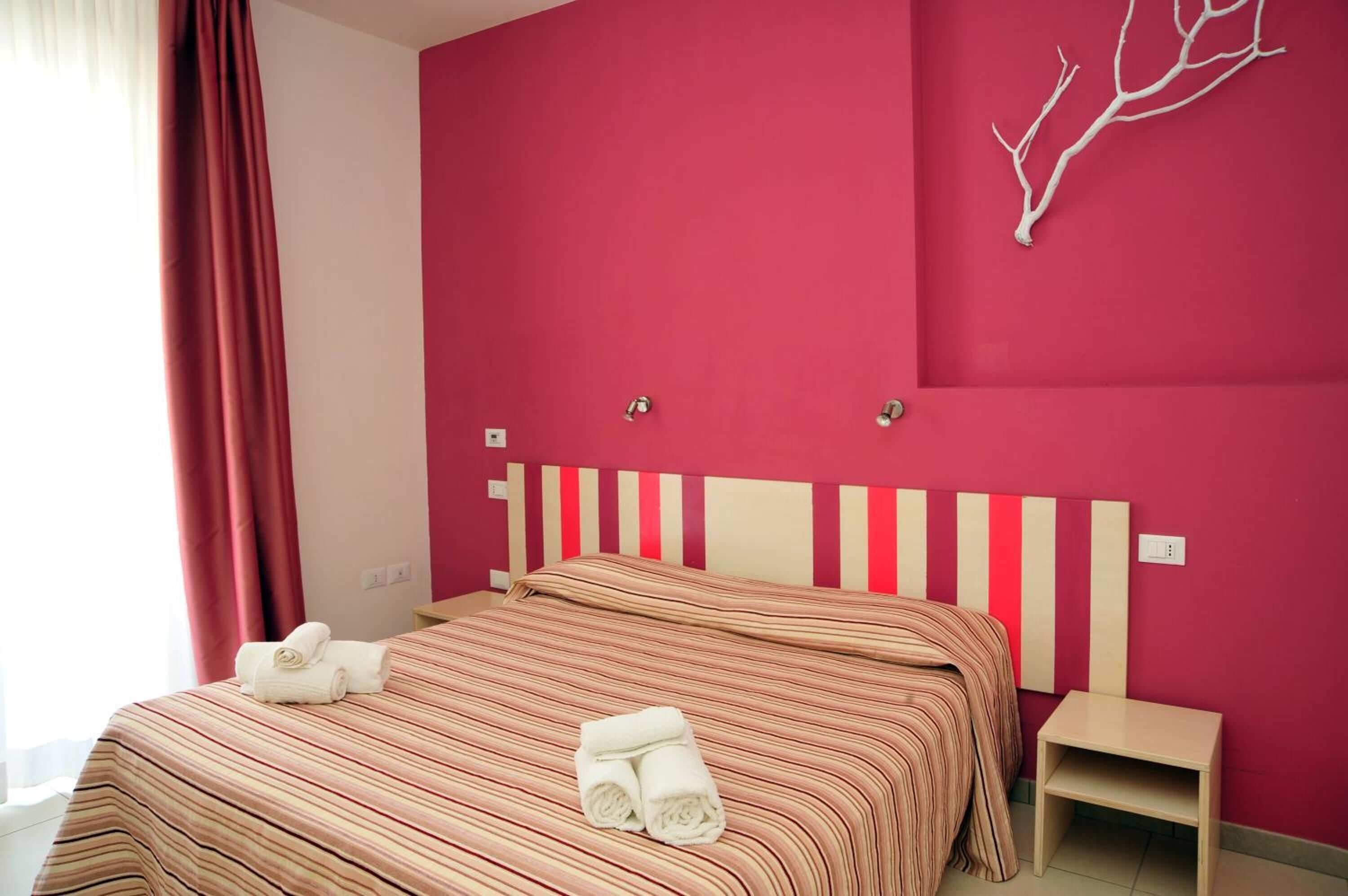 Una habitación de hotel con cama, mesita de noche y lámpara de pared.
