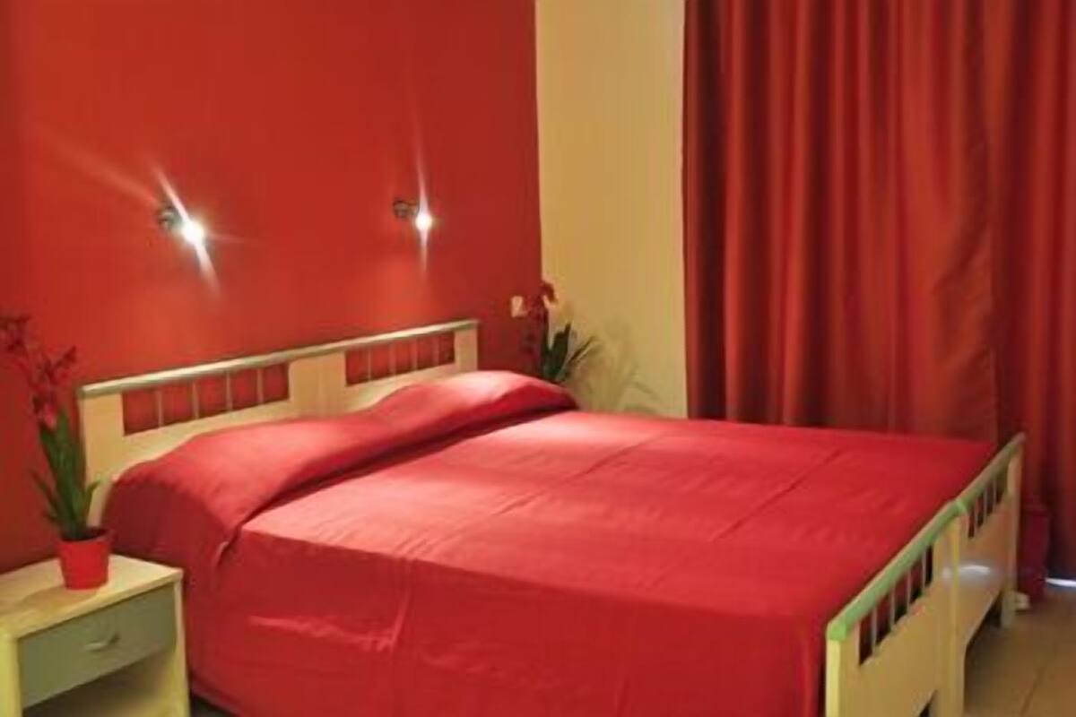 Cama com colcha vermelha em quarto com paredes e cortinas vermelhas.