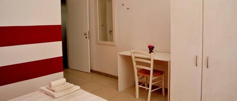 Una habitación de hotel con cama, escritorio, silla, armario y espejo.