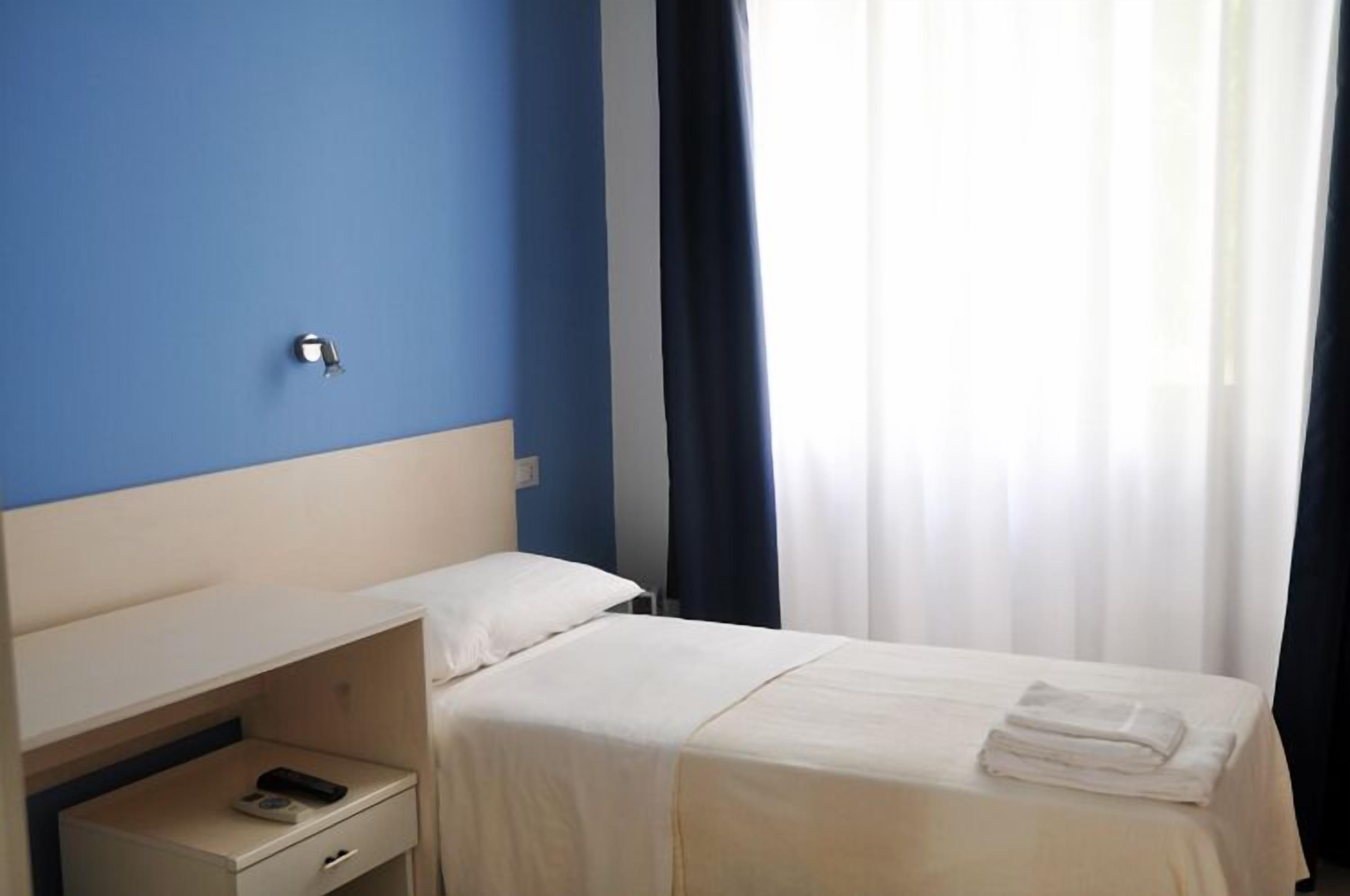 A hotel room with a bed, a nightstand, a phone, and a window with curtains.
