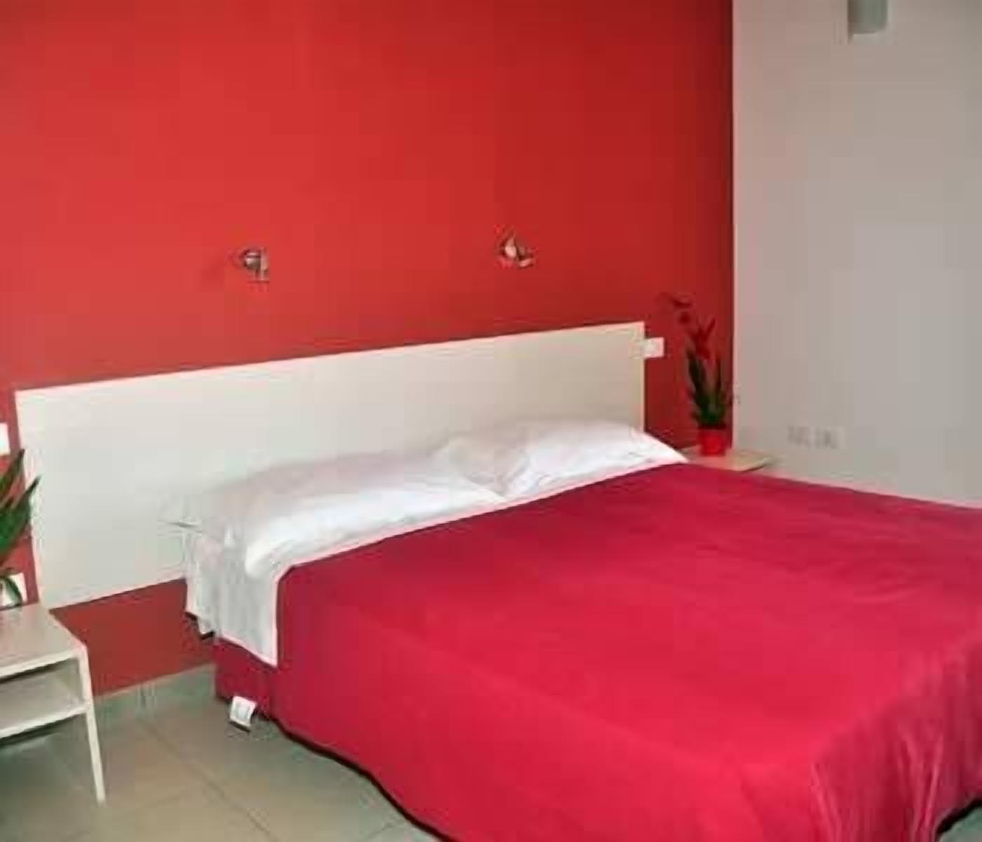 A bedroom with a white bed, red walls, and a small table with a plant.