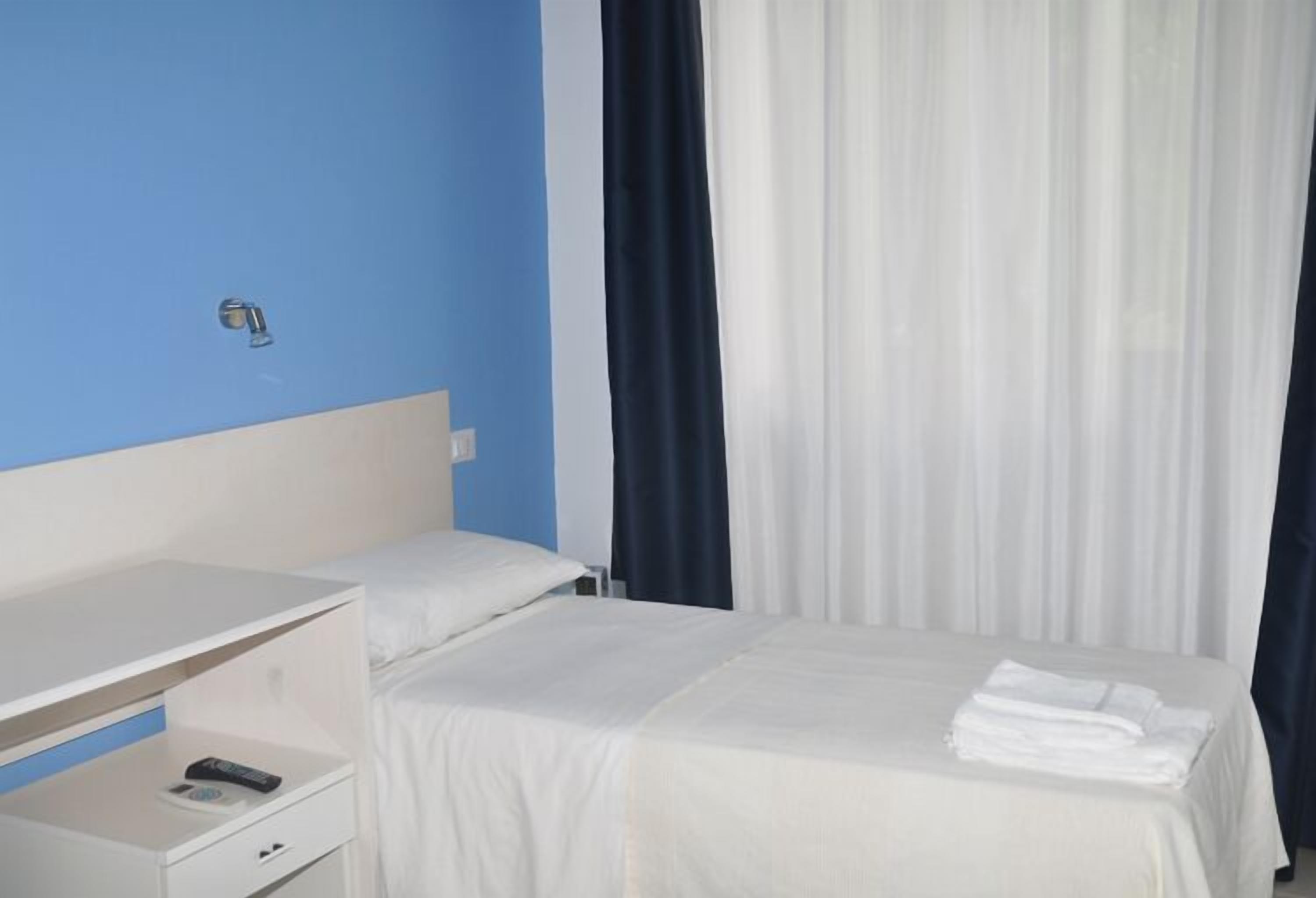 Une chambre d’hôtel avec un lit simple, une table de chevet et un petit bureau avec une chaise.