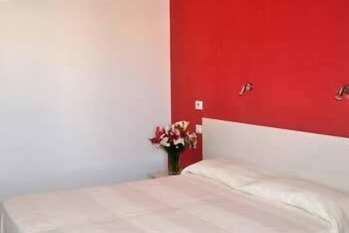 Uma cama de solteiro num quarto com uma parede de destaque vermelha e cabeceira branca.