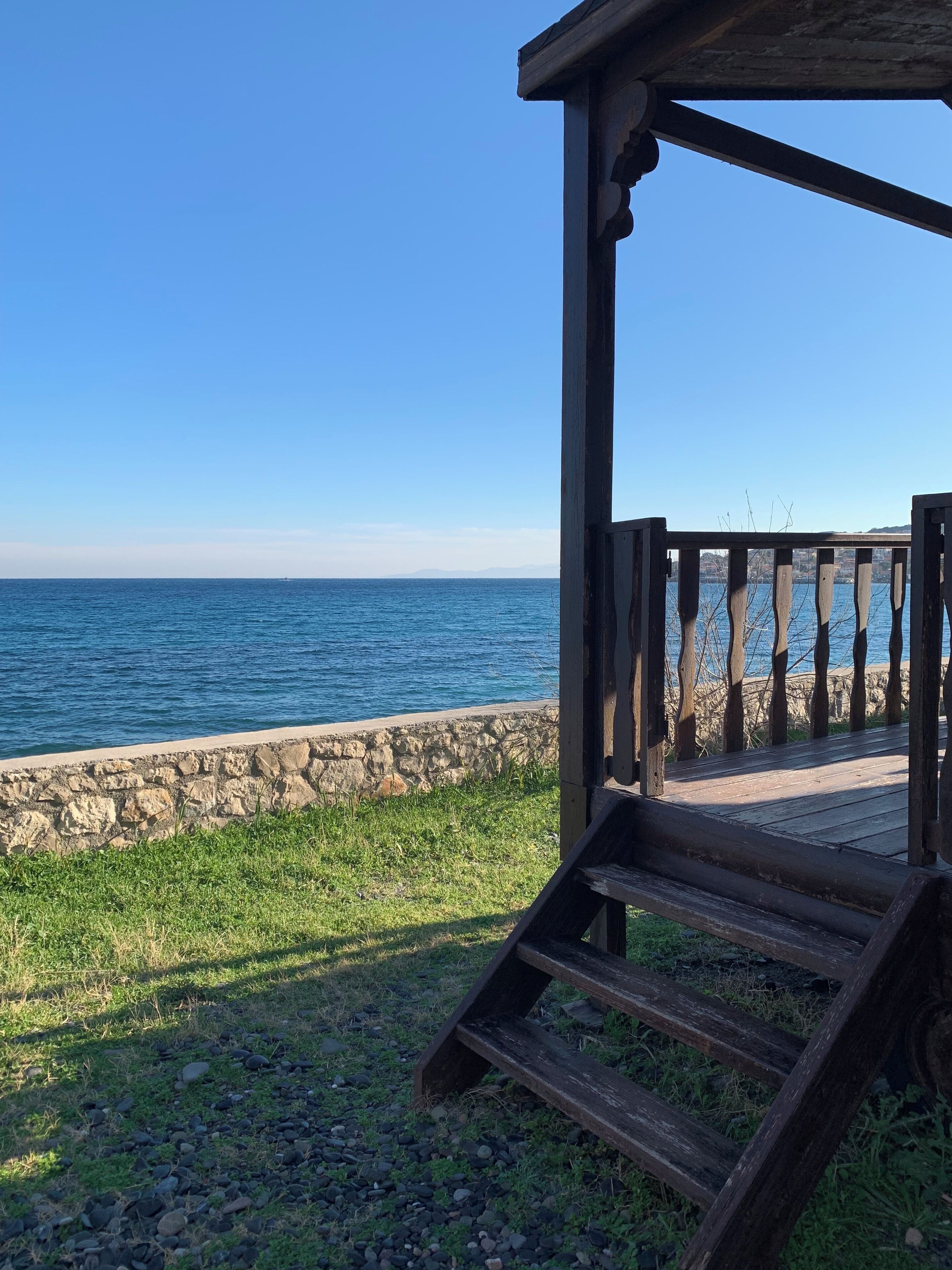 A wooden deck with a stone wall and a view of the sea.