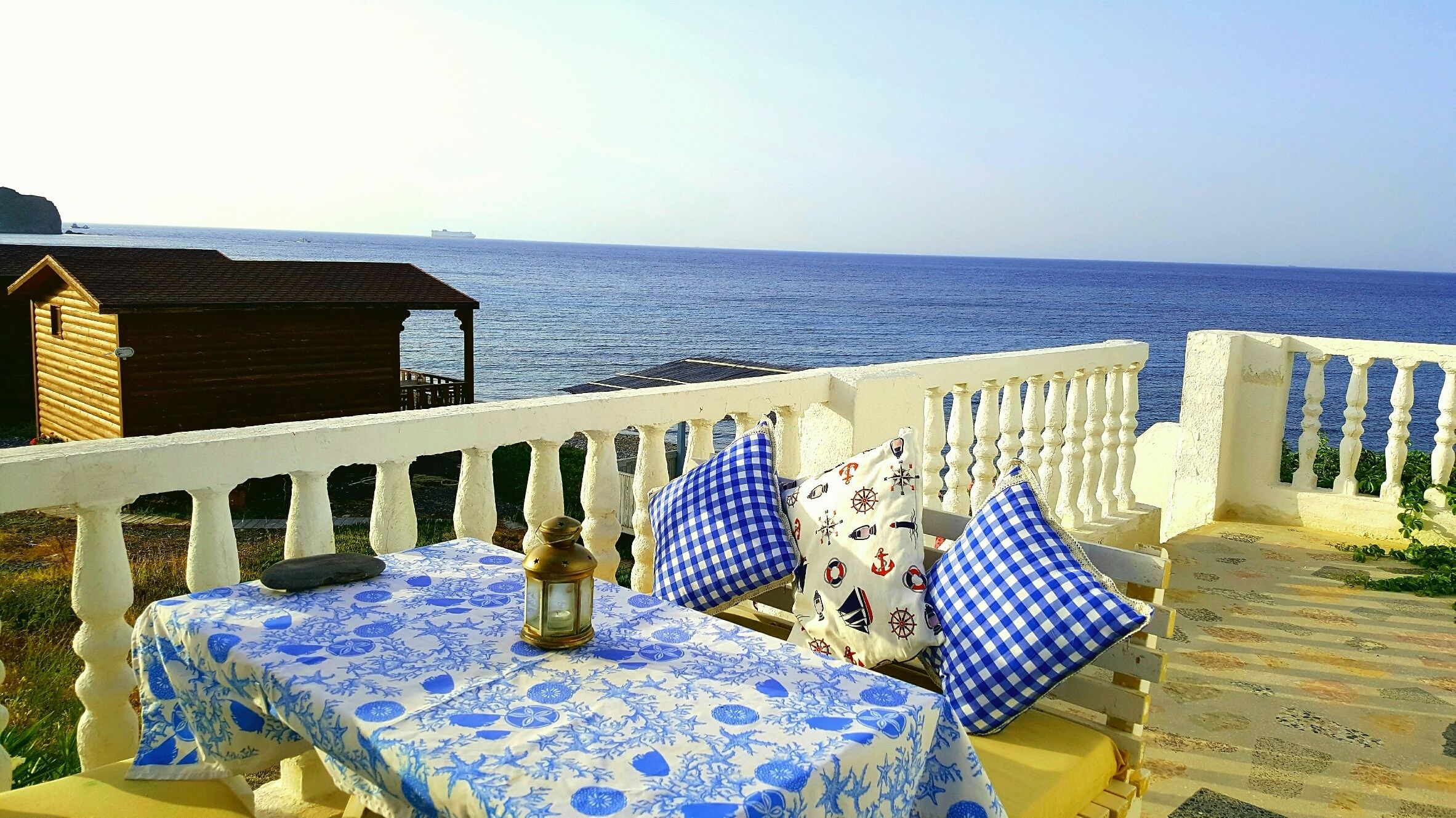 Une terrasse en bord de mer avec une table dressée pour deux personnes, une lanterne et une vue sur la mer.