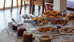 A buffet table with various food items and condiments, set in a room with large windows and wooden chairs. - Lipsos Hotel Ata's Place (Karaburun)