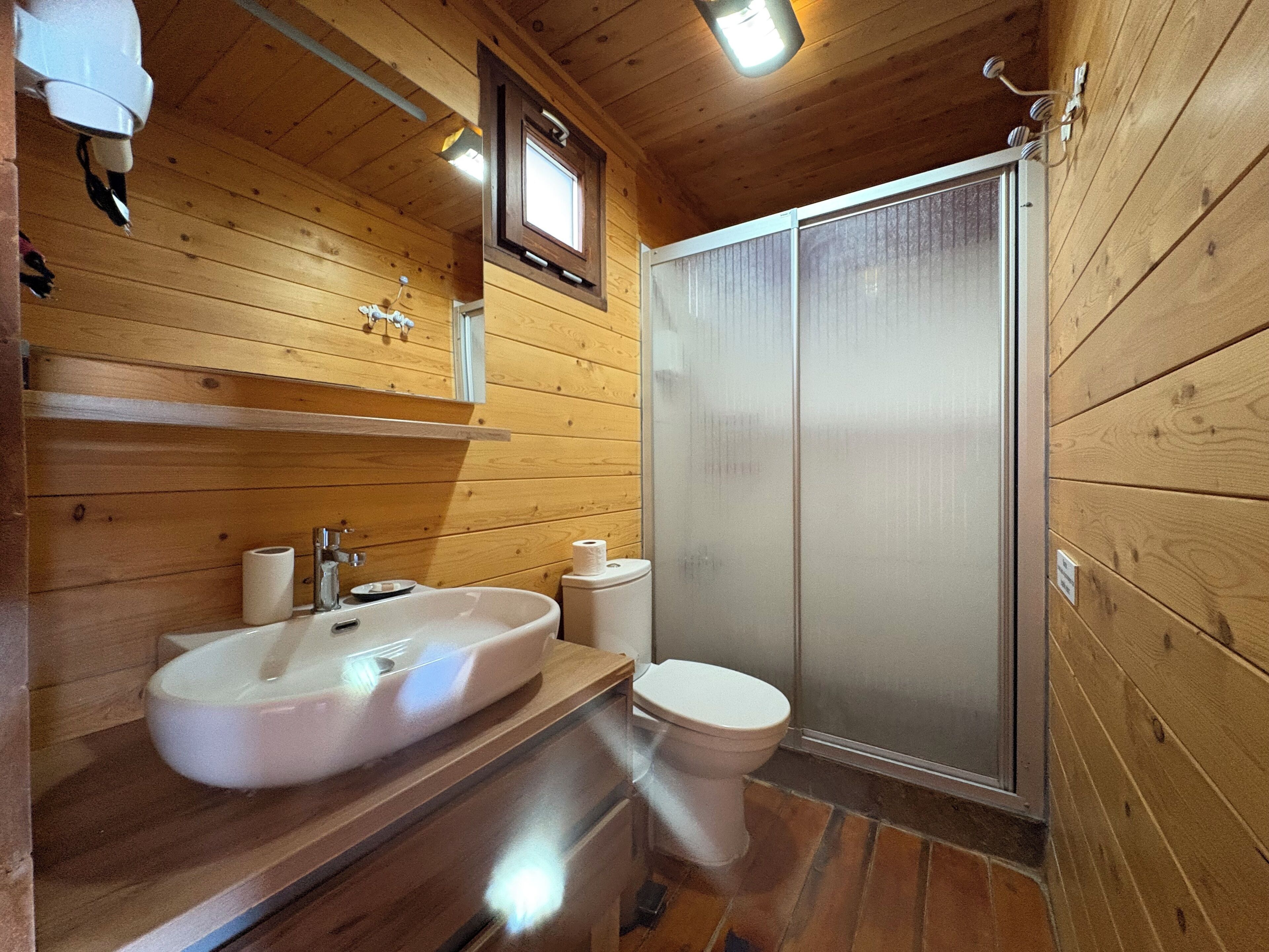 A wooden cabin bathroom with a sink, toilet, and a shower stall.