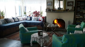 A cozy living room with a fireplace, a sofa set, and a bookshelf. - Lipsos Hotel Ata's Place (Karaburun)