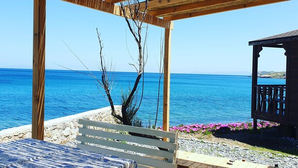 A wooden pergola with a view of the sea, a white bench, and a table with a blue and white tablecloth. - Lipsos Hotel Ata's Place (Karaburun)