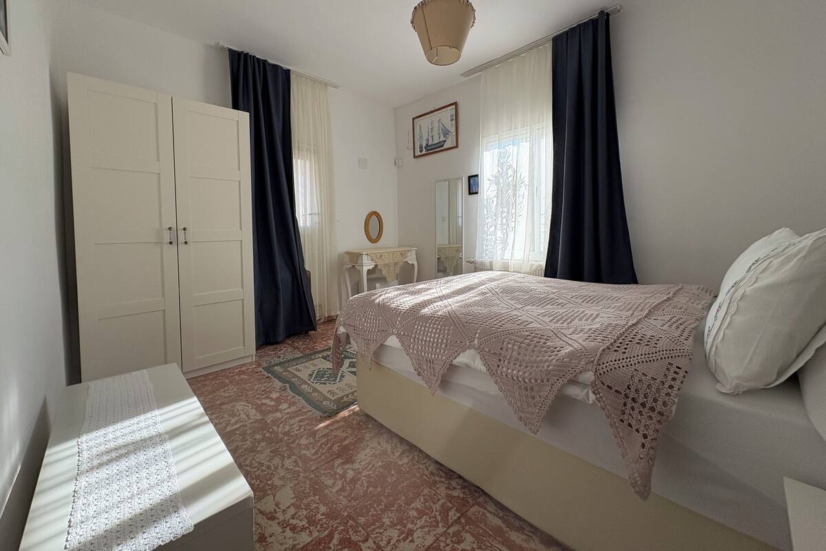 A bedroom with a bed, a nightstand, a dresser, and a window with curtains.