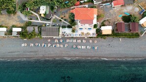 An aerial view of a coastal property with a large building, a parking area, and a beach. - Lipsos Hotel Ata's Place (Karaburun)