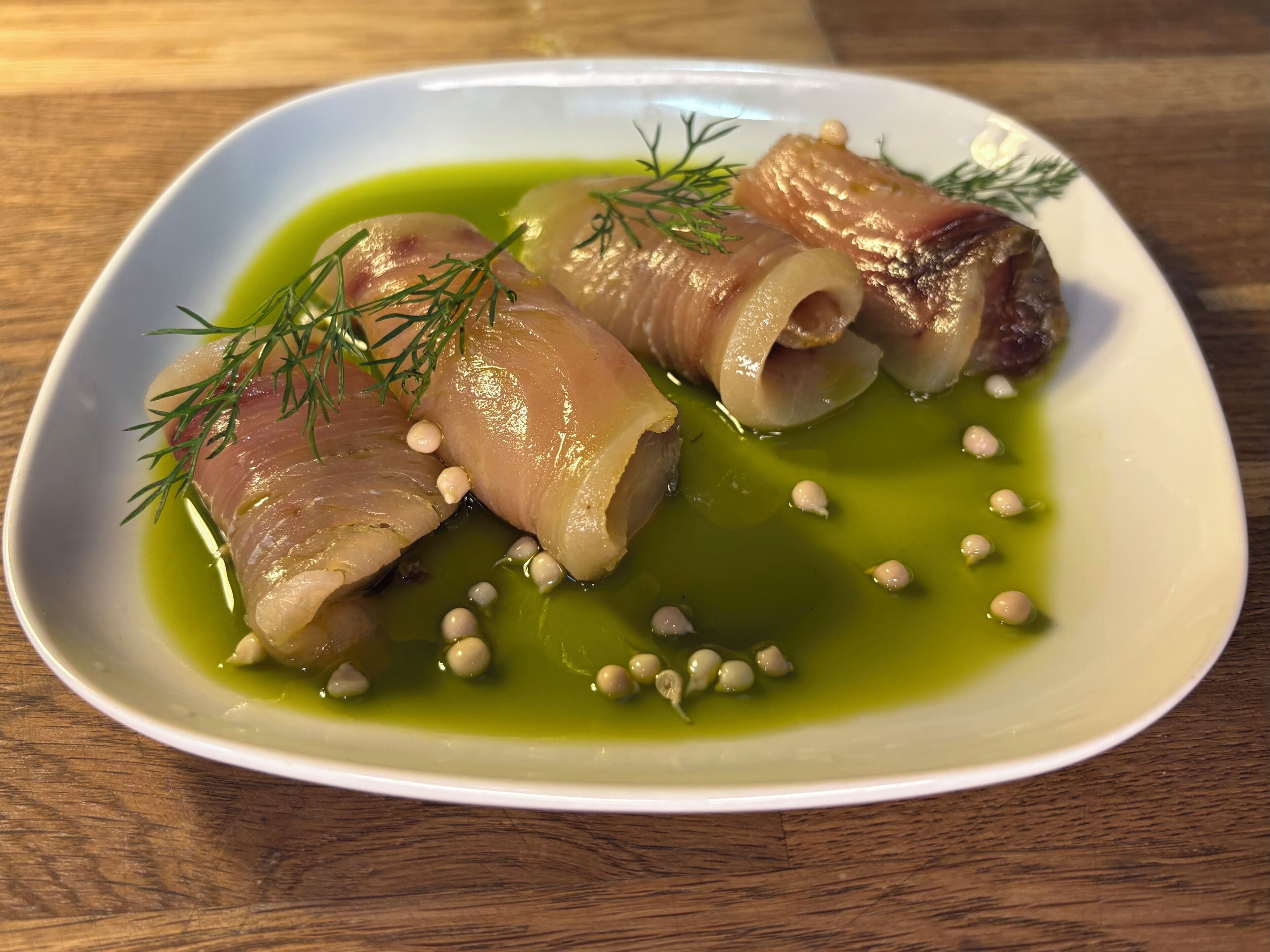 A plate of food with rolled meat and green sauce, garnished with dill and small white beads.