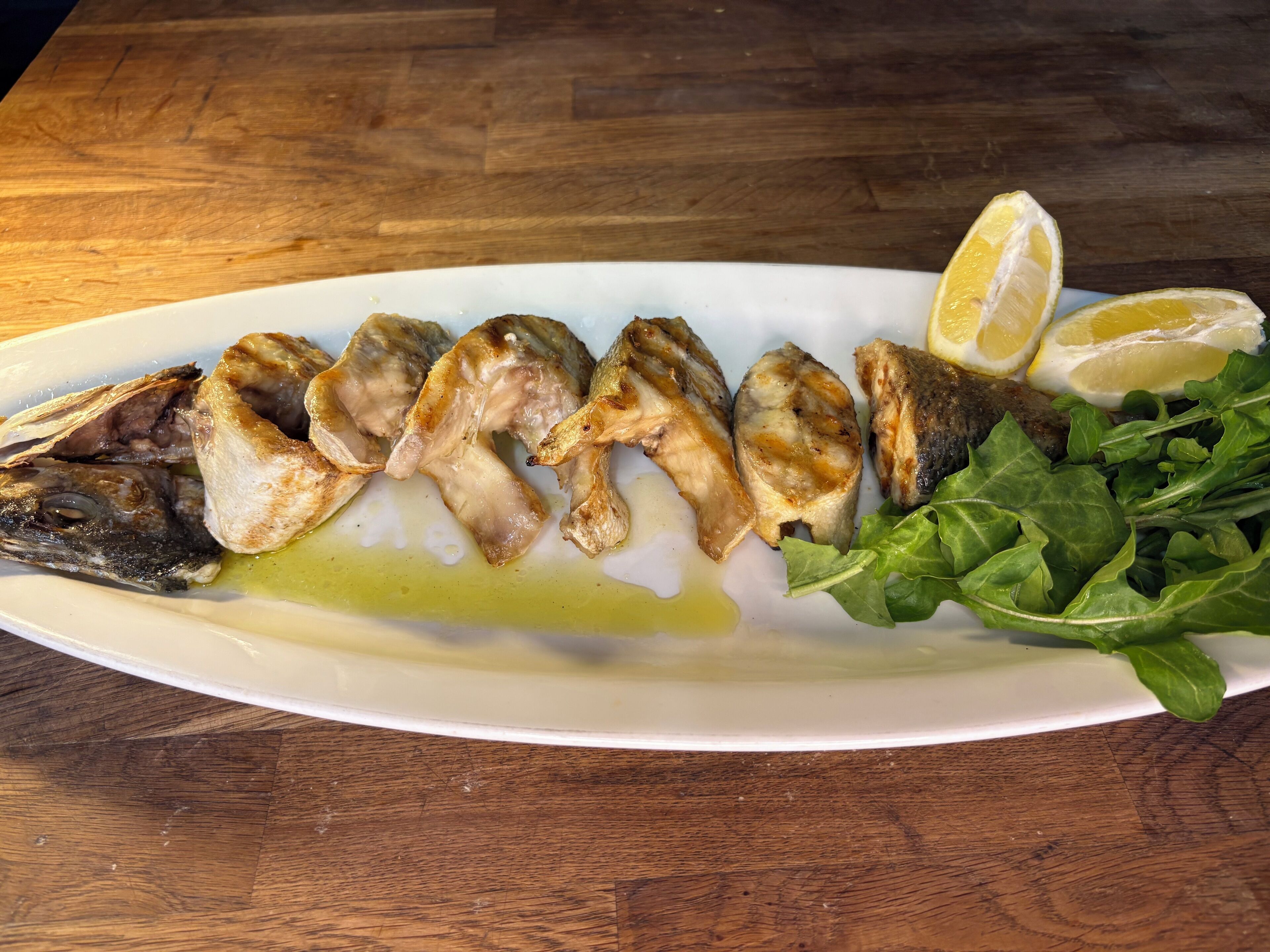 En tallerken med grillet fisk, citronskiver og grønt.