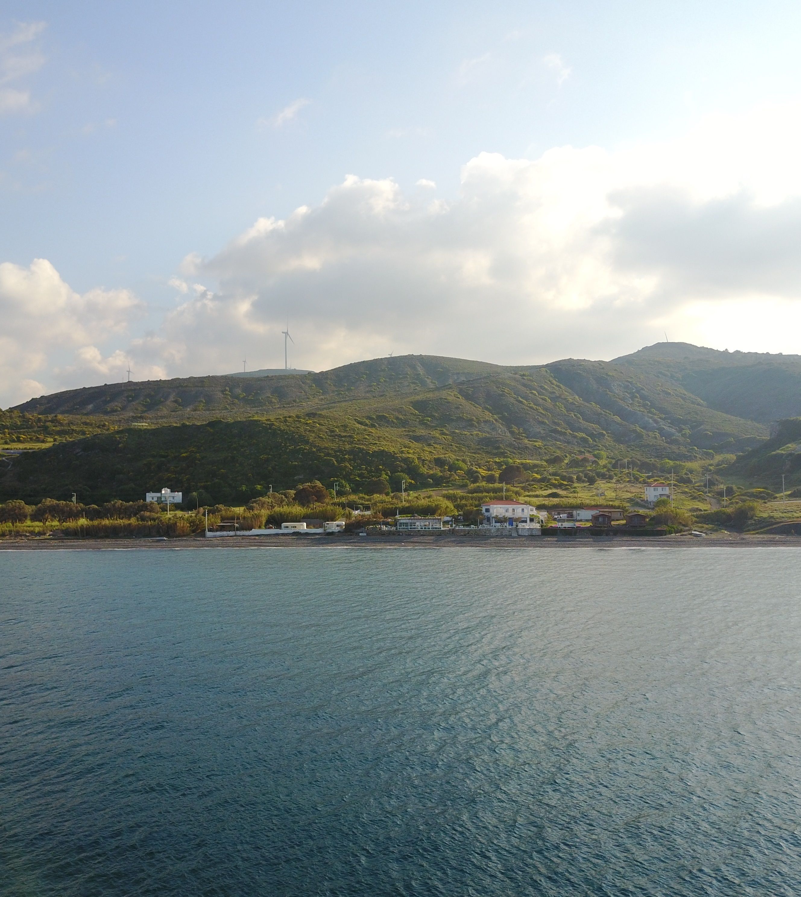 A coastal landscape with a view of a hillside, a body of water, and several buildings.
