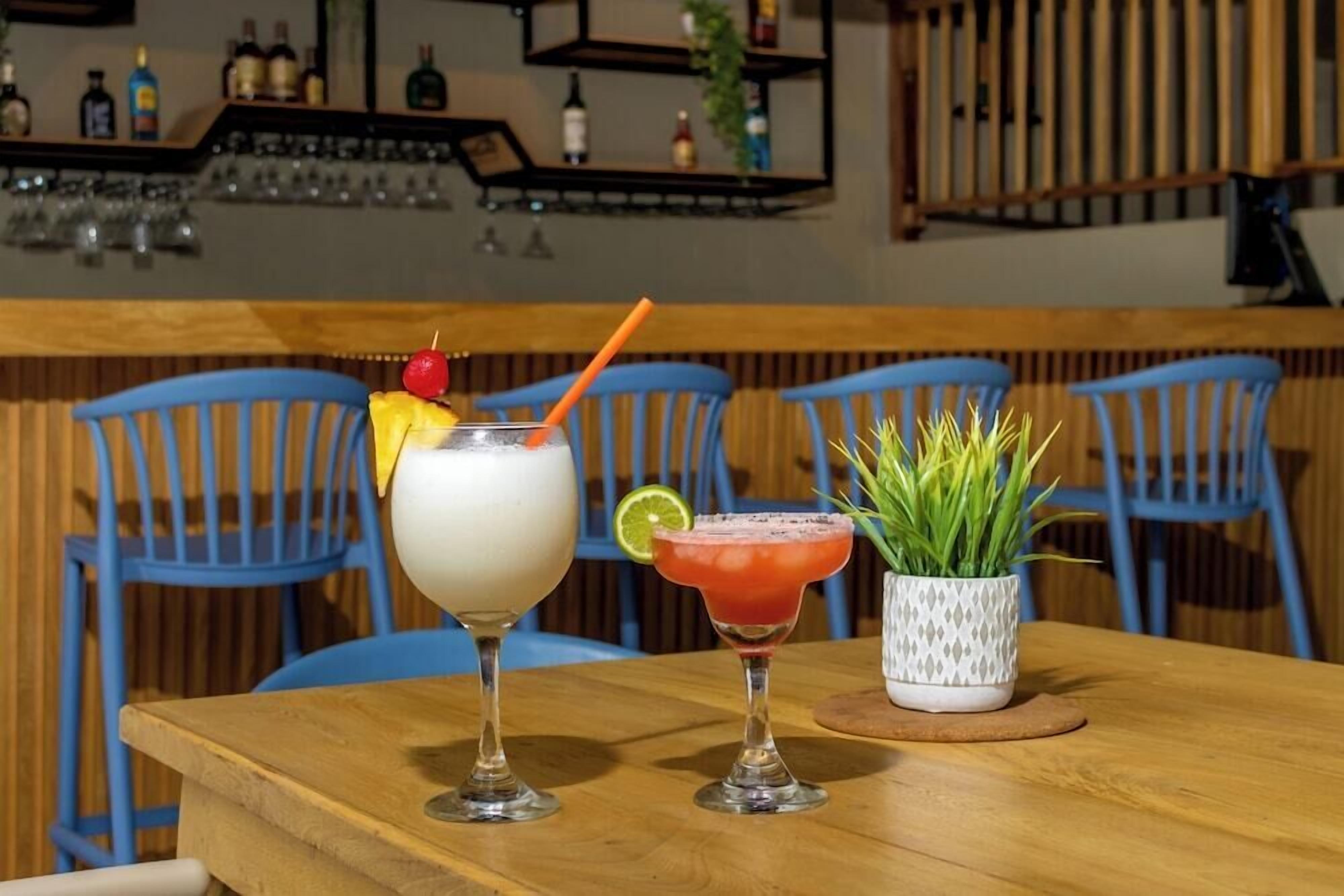 Two cocktails on a wooden table with blue chairs in the background.