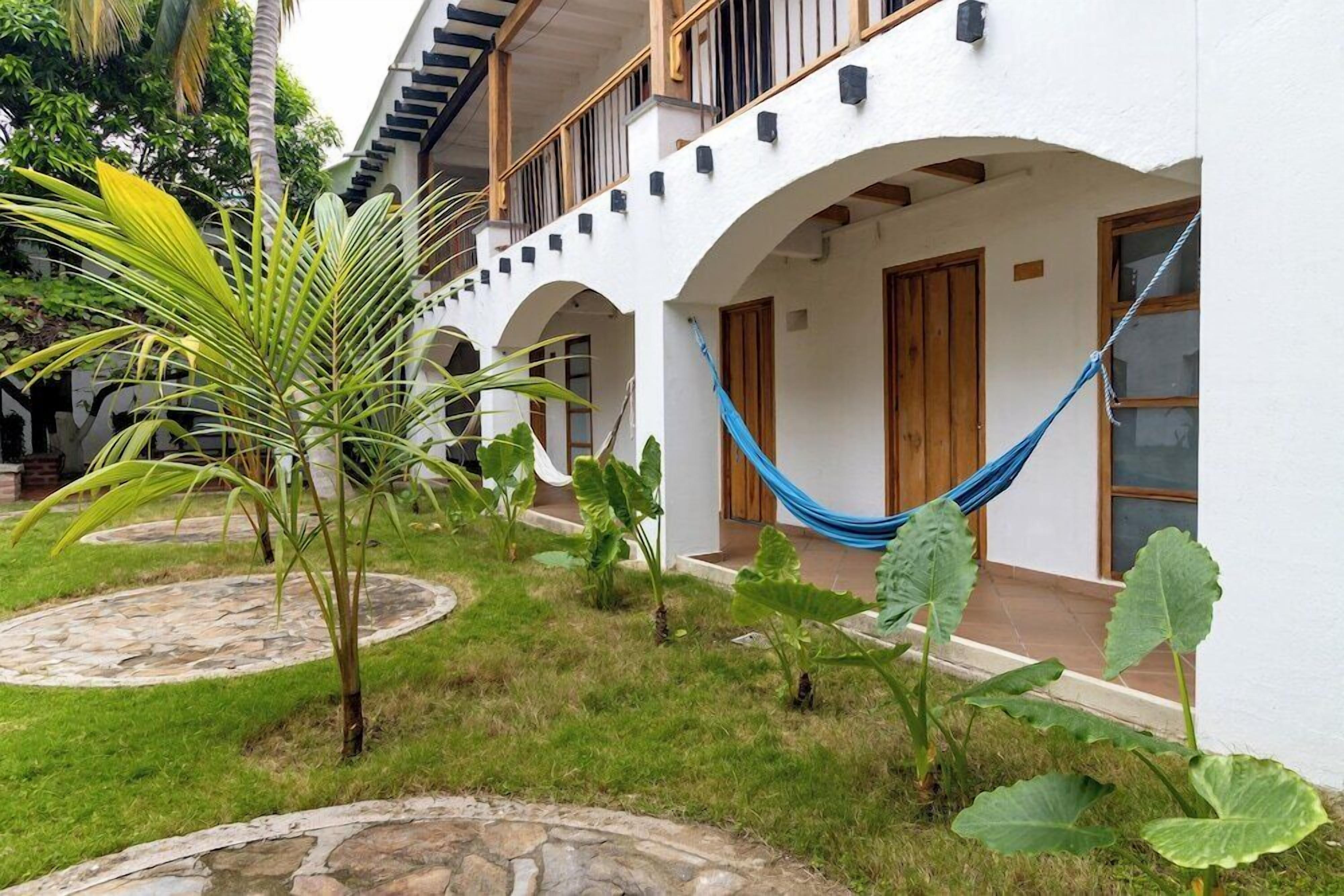 A white building with a covered patio, stone pathways, and a hammock.