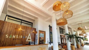 A hotel reception area with a wooden reception desk, large columns, and hanging wicker lamps. - Sansiraka (Santa Marta)