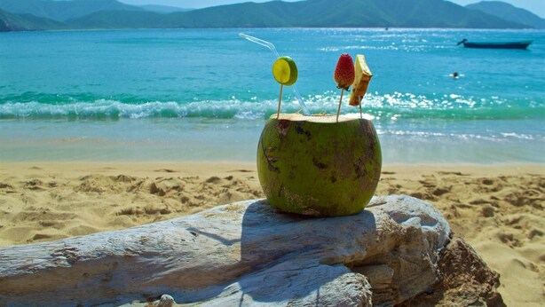 A beach scene with a coconut drink on a rock, clear blue water, and distant mountains. - Sansiraka (Santa Marta)