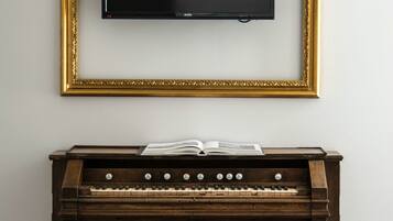Un piano de madera oscura con partituras, un marco dorado para fotografía y un televisor negro montado en una pared blanca.