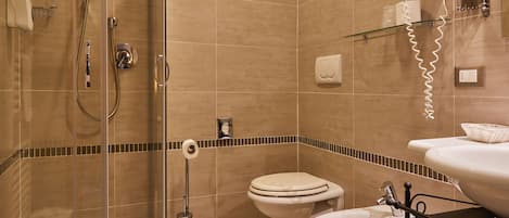 Un baño con ducha de mampara de vidrio, dos inodoros, un bidé y un lavabo.