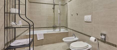 A modern bathroom with a bathtub, shower, toilet, and a metal shelf with towels.