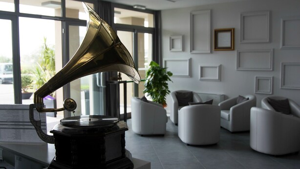 Un salón moderno con un tocadiscos sobre un pedestal blanco, sofás blancos y un ventanal con vistas al exterior.