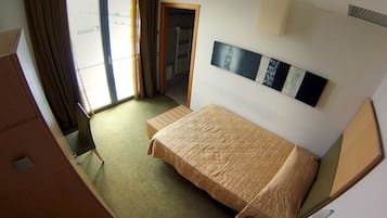 A hotel room with a bed, a desk, a chair, a window with curtains, and a door leading to a bathroom.