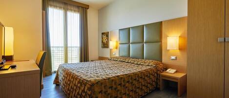 Quarto de hotel com uma cama grande, uma escrivaninha, uma cadeira, mesa de cabeceira com telefone e guarda-roupa.