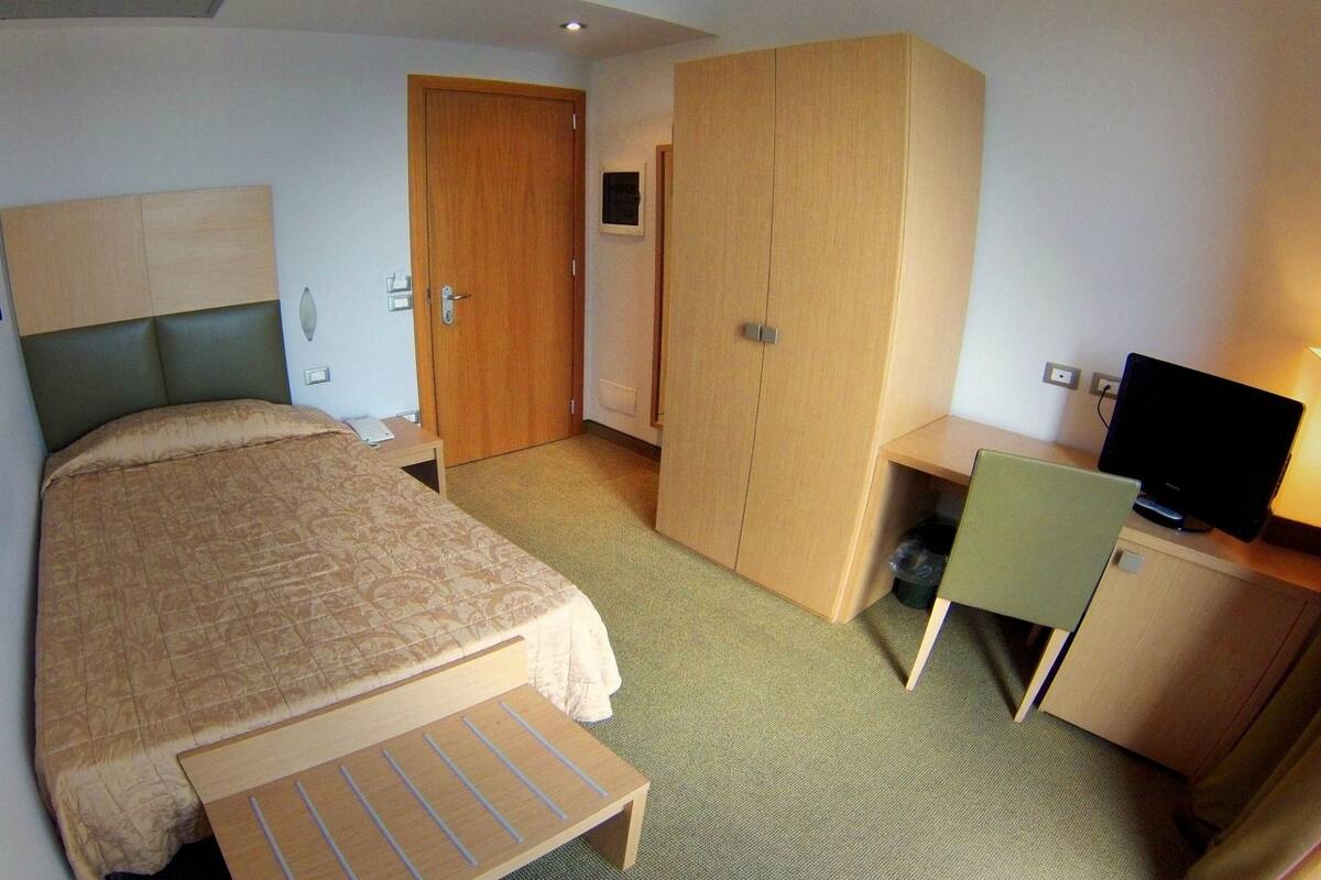 A hotel room with a bed, a desk with a chair, a television, and a wardrobe.