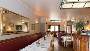 A restaurant with a long dining table set for a meal, a large mirror on the wall, and a stained glass window above. - Auberge le XIXème (Hensies)
