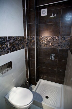 A bathroom with a shower, toilet, and a tiled wall with a decorative pattern. - RG Status Hotel (Katerini)