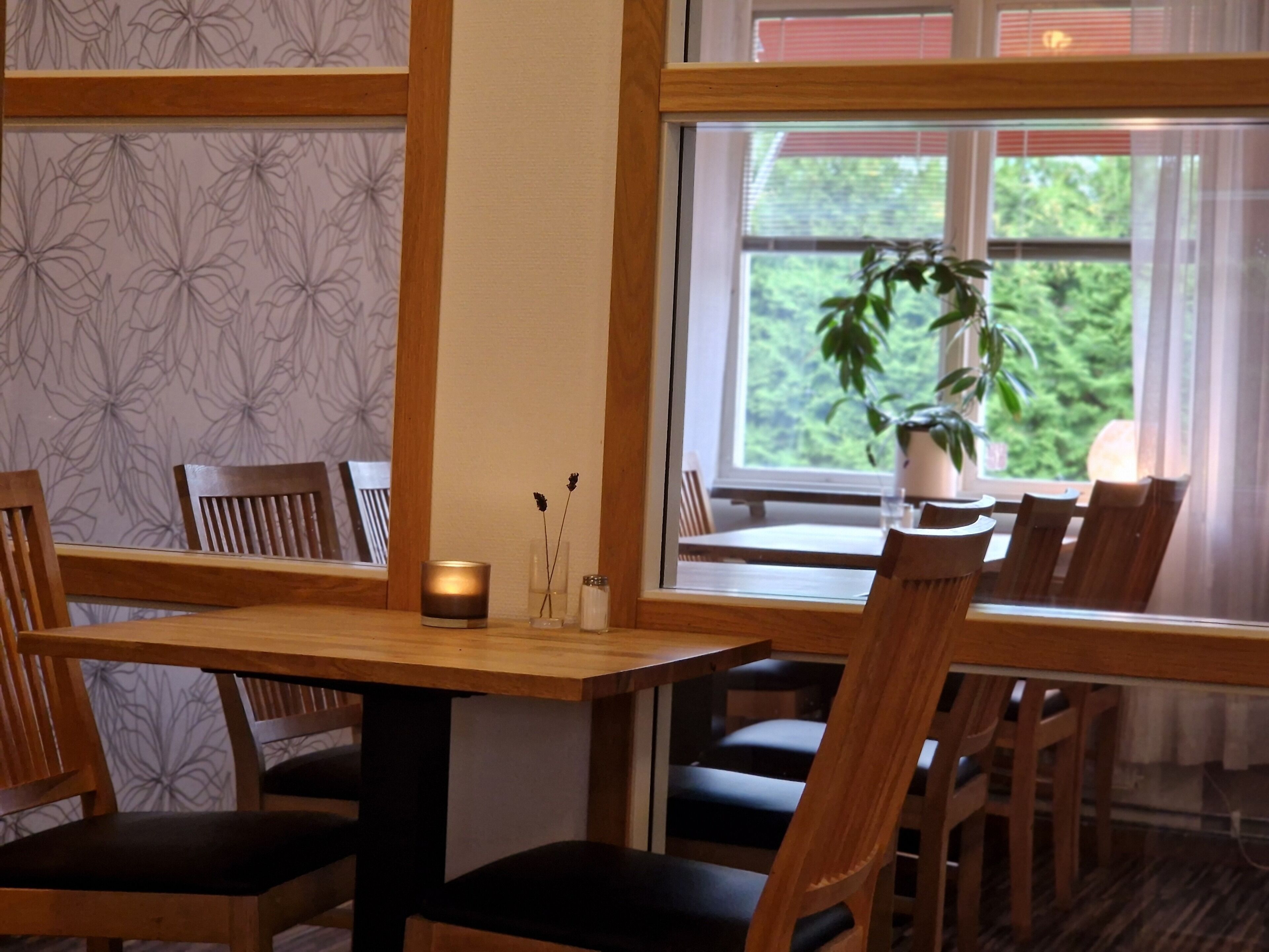 Un coin repas avec des meubles en bois, une table, des chaises, une bougie et une fenêtre donnant sur un paysage verdoyant.