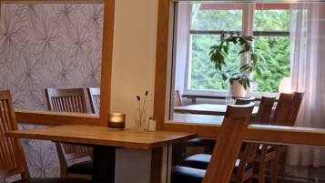 Un coin repas avec des meubles en bois, une table, des chaises, une bougie et une fenêtre donnant sur un paysage verdoyant.