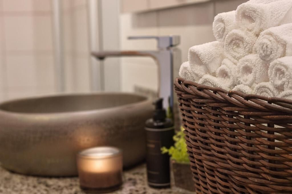 Un baño con un lavabo redondo, una cesta de mimbre con toallas, una vela y un dispensador de jabón.