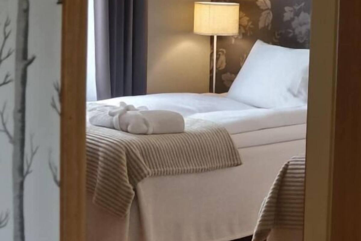 Quarto de hotel com cama, mesa de cabeceira, abajur e papel de parede floral.
