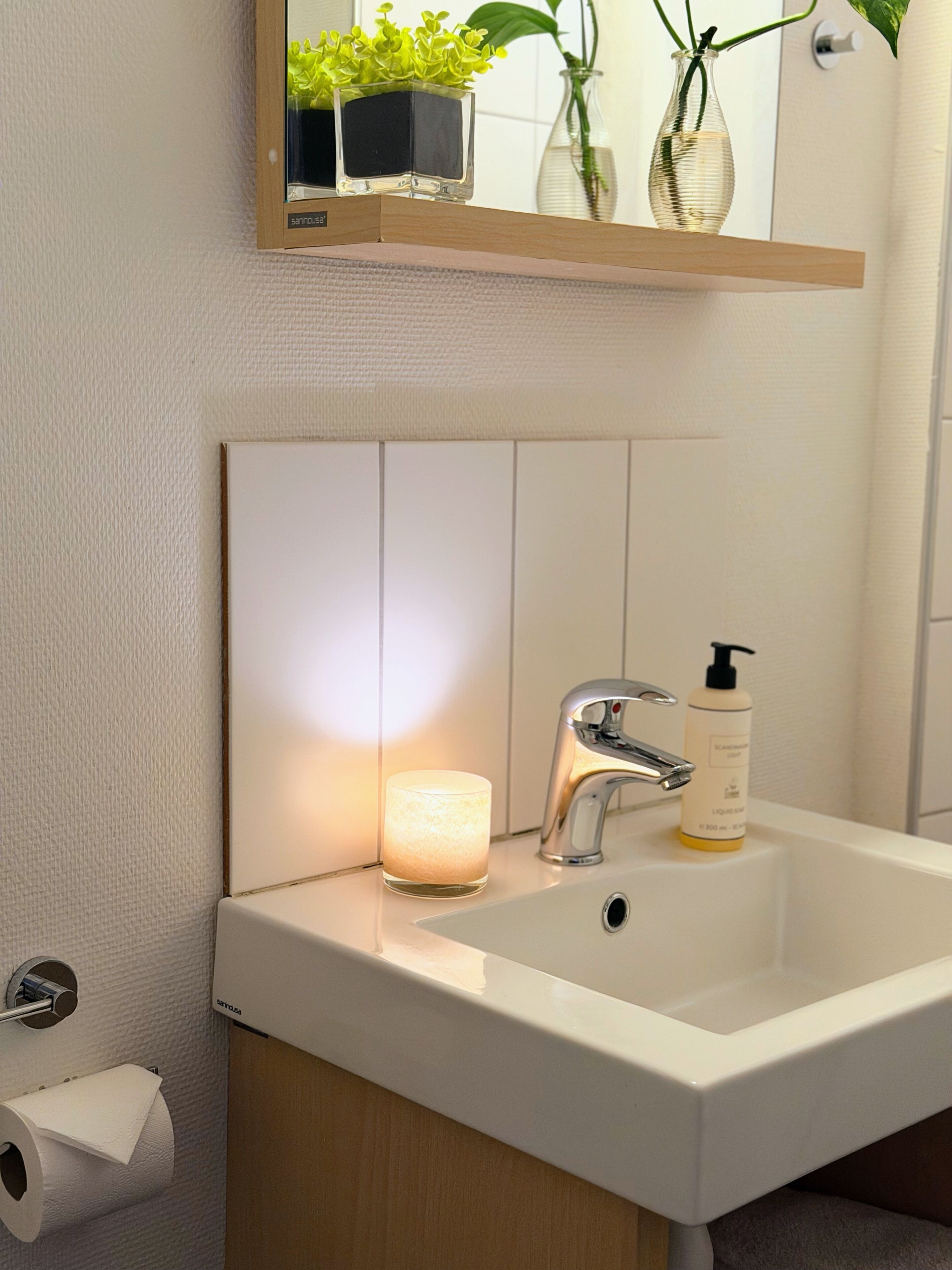 A bathroom with a white sink, a mirror above it, a candle, and a bottle of liquid soap.