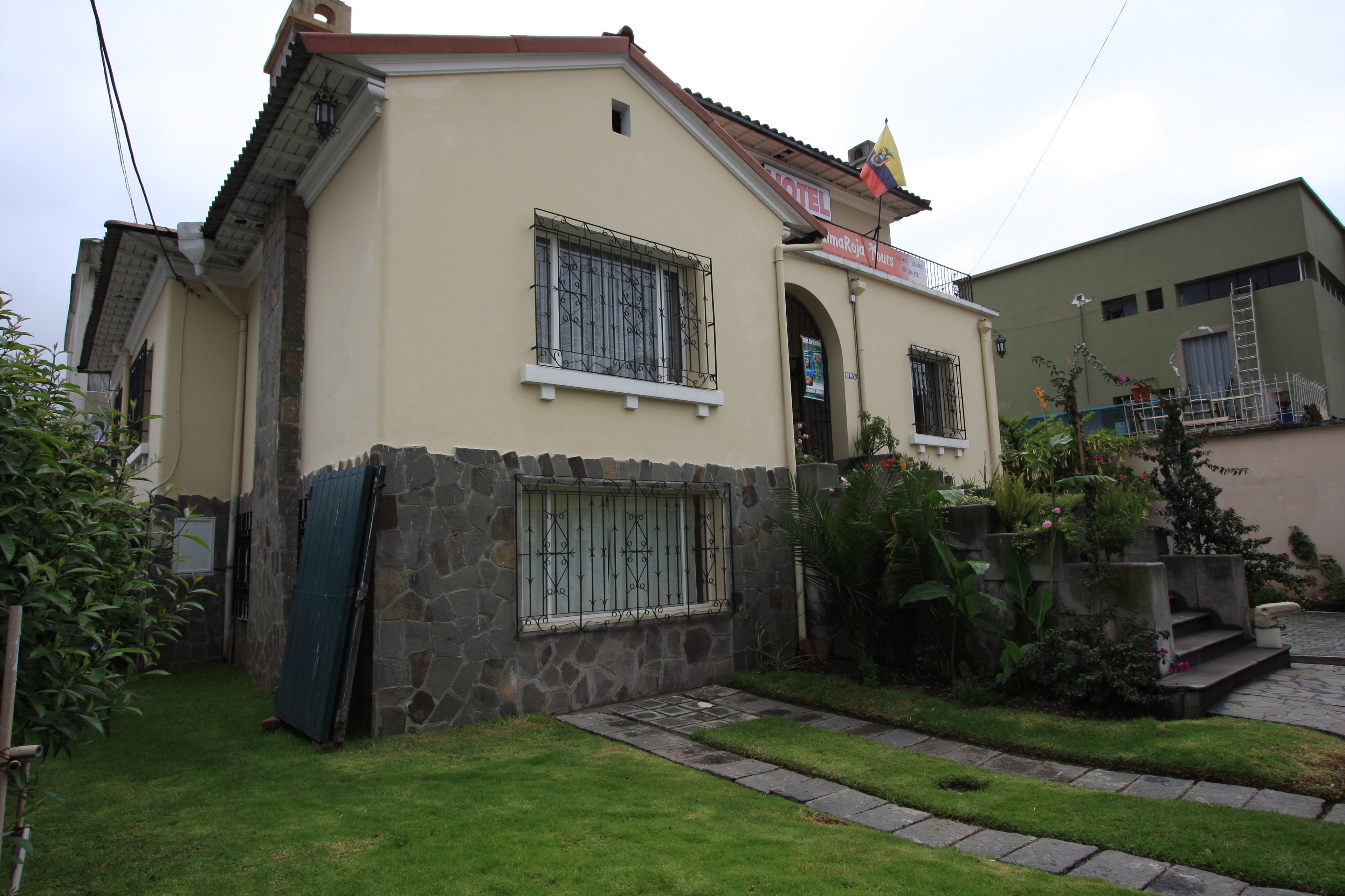 Un bâtiment à deux étages, doté d’une façade en pierre, d’un toit en tuiles et d’un petit jardin agrémenté d’un sentier menant à l’entrée.