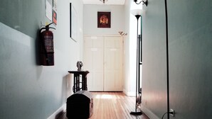 Un couloir avec un plancher en bois, un tapis noir, une machine à coudre, un extincteur et une lampe sur pied.