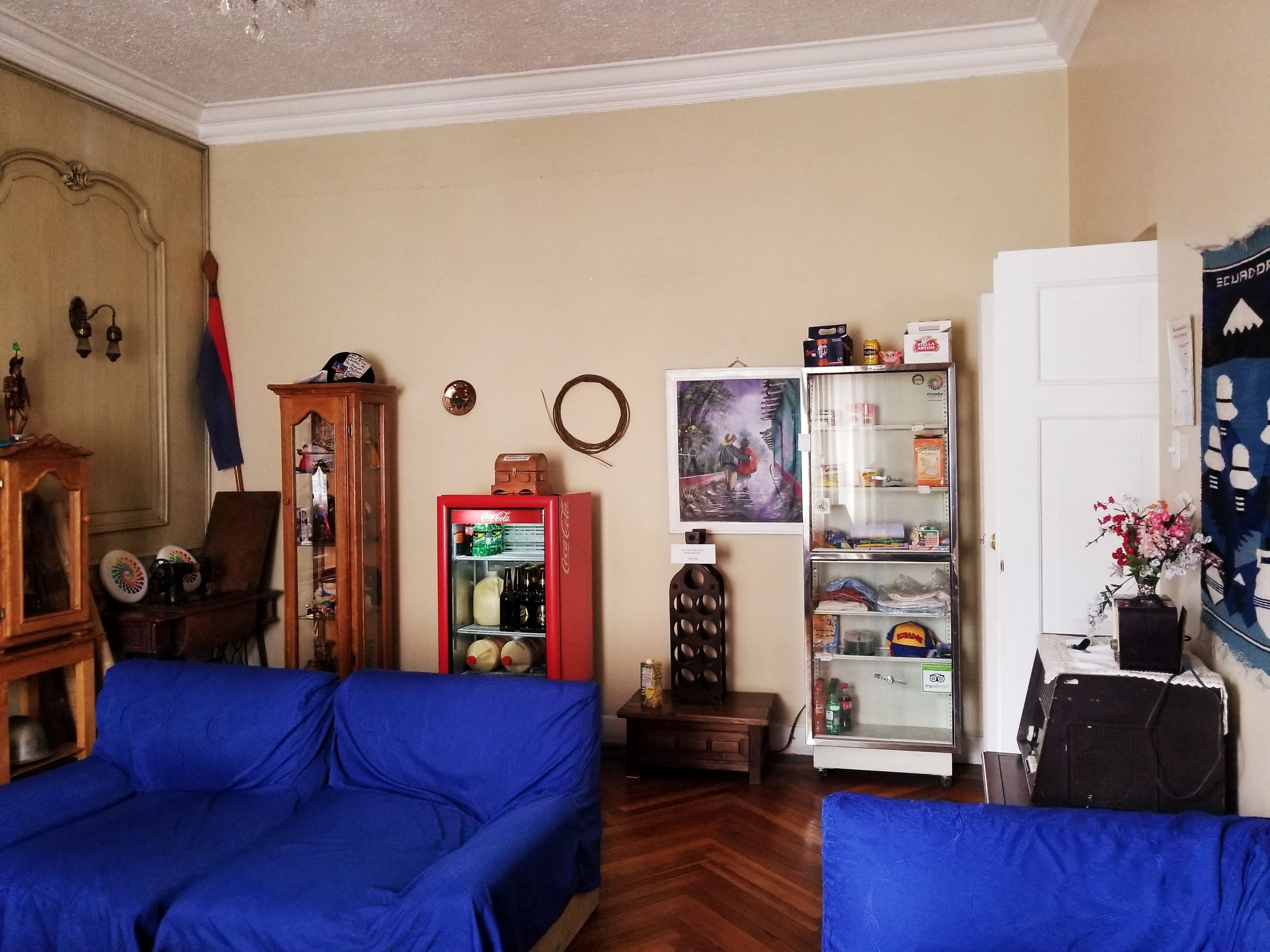 Una sala de estar con un sofá azul, un refrigerador, un armario de madera y un cuadro en la pared.