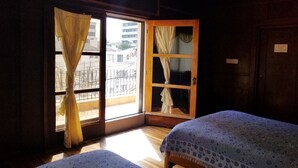 Une chambre avec deux lits, une porte en bois et une vue sur les bâtiments environnants.
