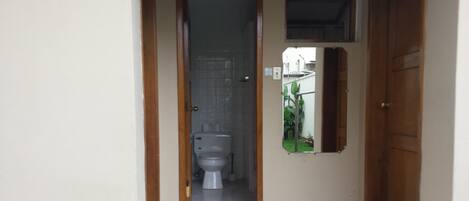 Een badkamer met een toilet, een klein raam en een deur.