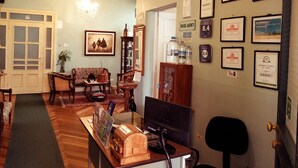 Un salon chaleureux avec une cheminée, un lustre, un canapé, une table basse et un bureau avec un ordinateur. Des trophées encadrés ornent le mur, et une grande fenêtre offre une vue imprenable.