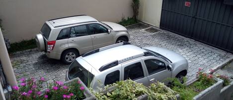 A parking area with two SUVs parked next to a building with a tiled roof and a sign reading "MULTISERVICIOS".