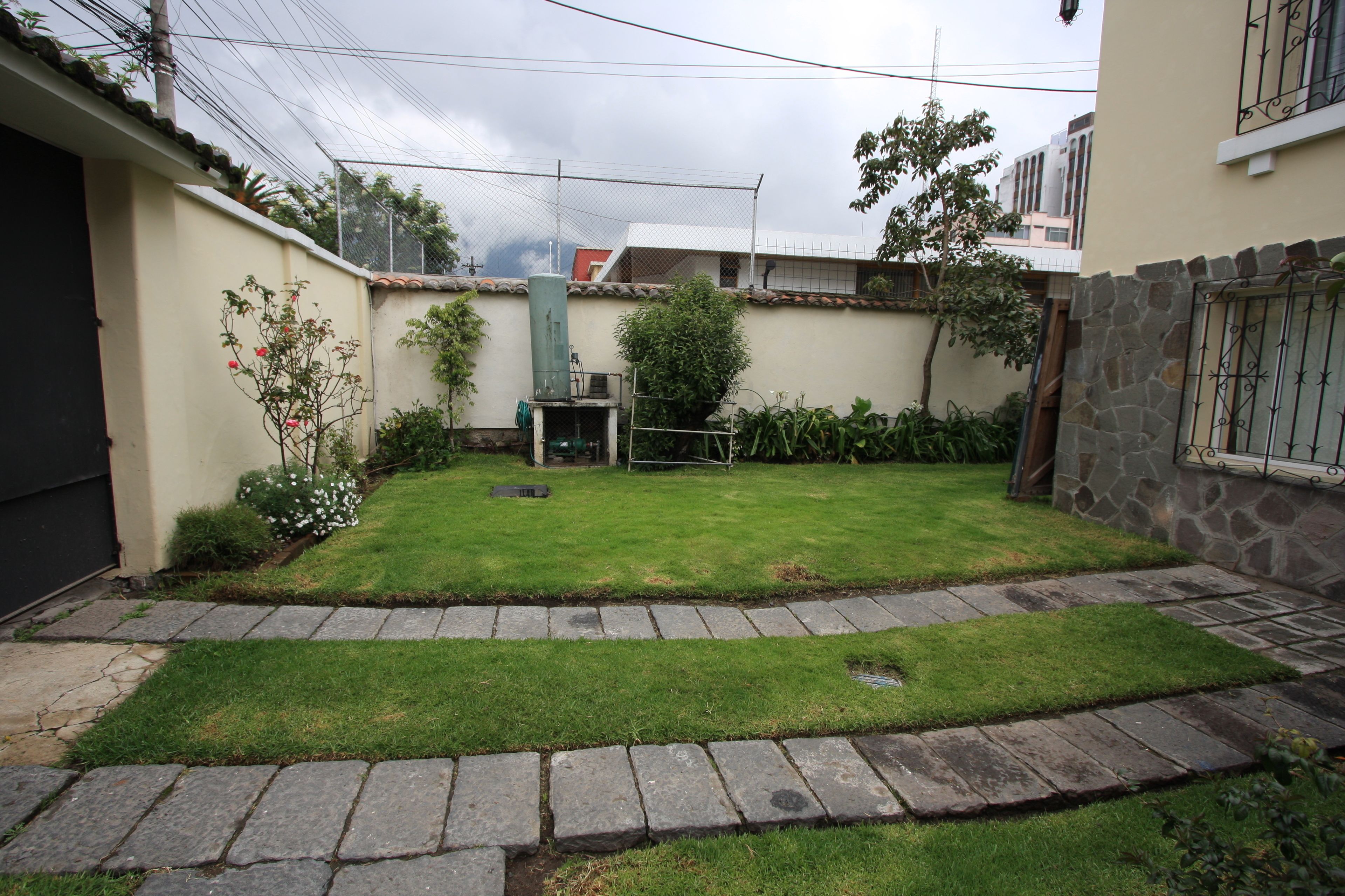 A courtyard with a grassy lawn, stone pathway, and a fenced area.